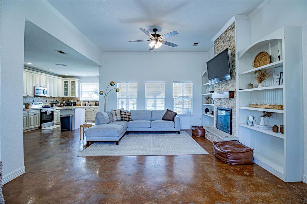 328 Meadow Lane Red Oak, TX 75154 - Photo 5 of 35 Living area with crown molding, a stone fireplace, concrete floors, a textured ceiling, and a ceiling fan