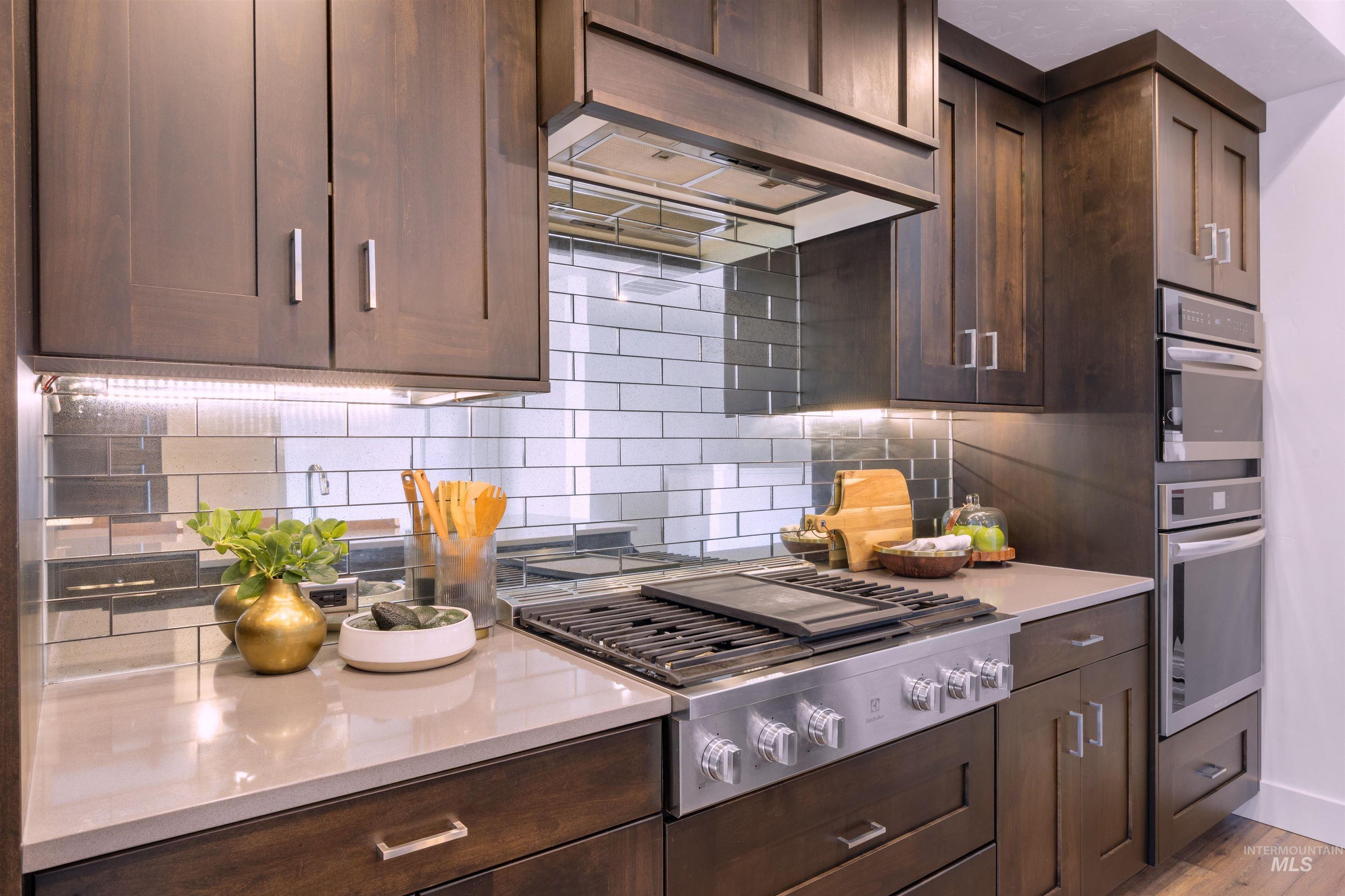 3282 South Millbrook Way Boise, ID 83716 - Photo 22 of 45 Kitchen with dark wood finish cabinets, extractor fan, stainless steel appliances, decorative backsplash, and light stone counters