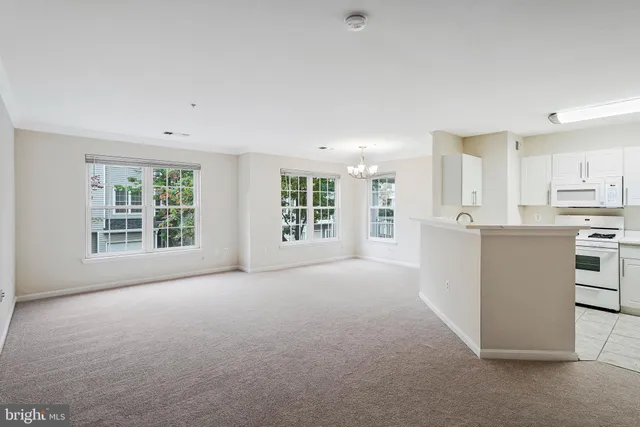 a view of an empty room with kitchen and window