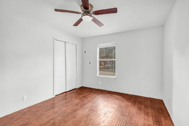 an empty room with wooden floor ceiling fan and windows