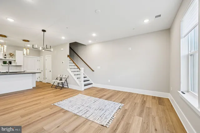 a view of an empty room with wooden floor and kitchen view