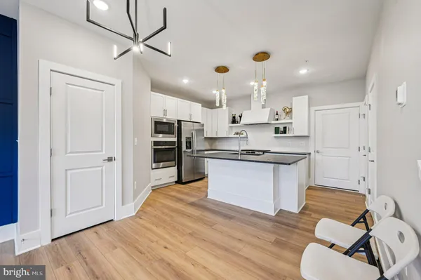 a large kitchen with kitchen island a stove a sink dishwasher a refrigerator and white cabinets with wooden floor