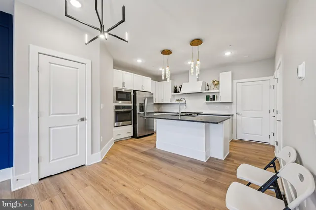 a large kitchen with kitchen island a stove a sink dishwasher a refrigerator and white cabinets with wooden floor