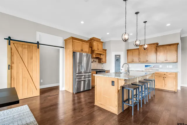 a kitchen with stainless steel appliances granite countertop a refrigerator a oven a sink a dining table and chairs with wooden floor