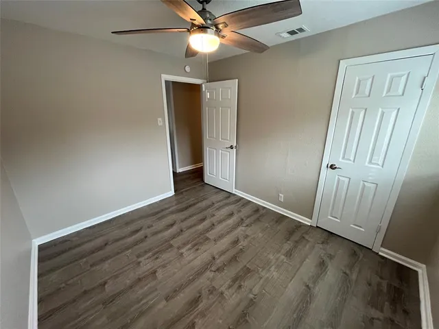 an empty room with wooden floor fan and windows