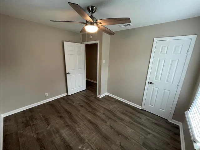 an empty room with wooden floor fan and windows