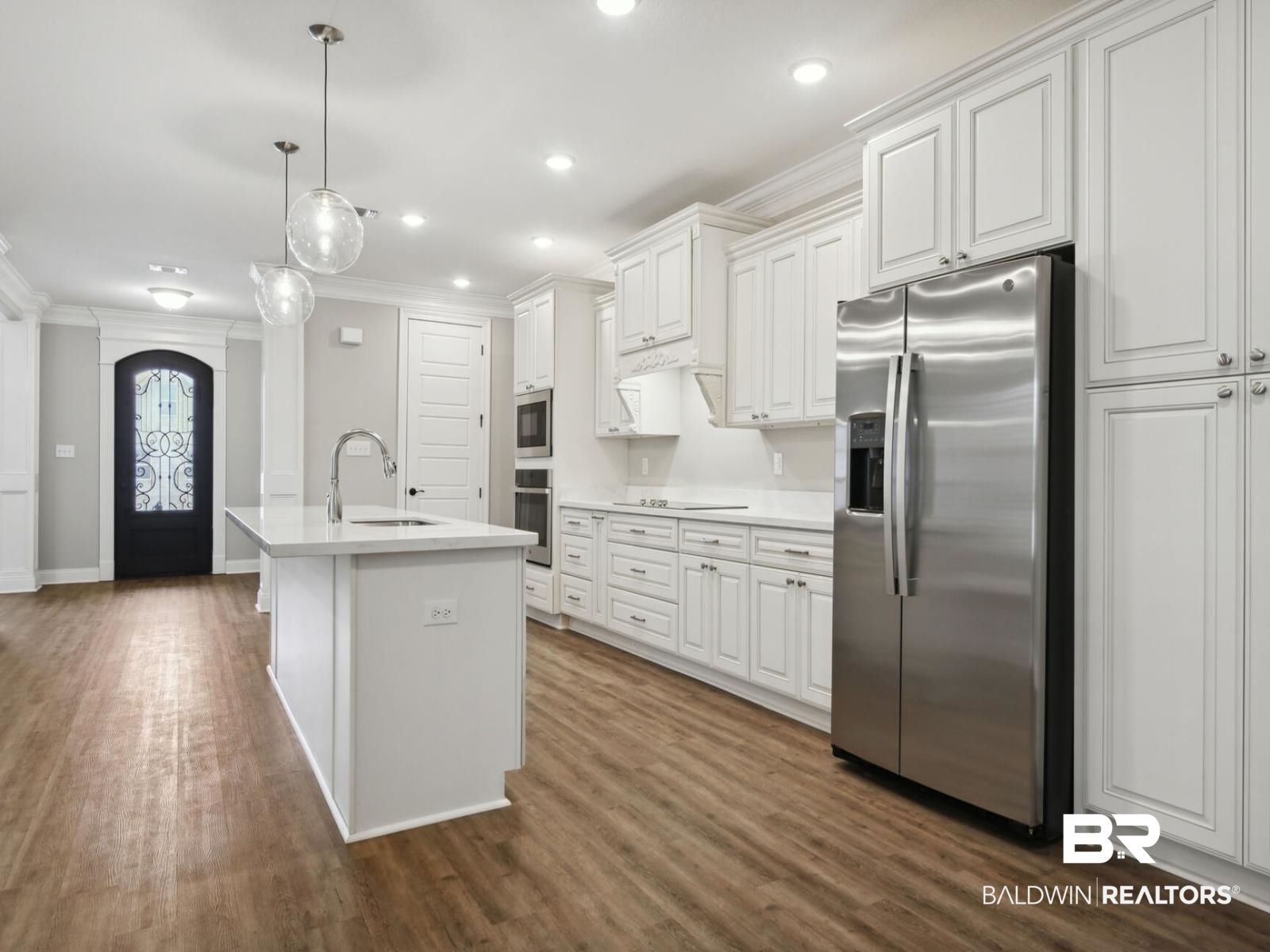 12942 Gondala Street Elberta, AL 36530 - Photo 3 of 18 Kitchen featuring stainless steel appliances, crown molding, white cabinetry, decorative light fixtures, and a center island with sink