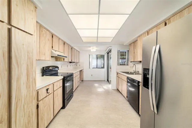 a large kitchen with stainless steel appliances granite countertop a refrigerator a sink dishwasher a stove and white cabinets with wooden floor