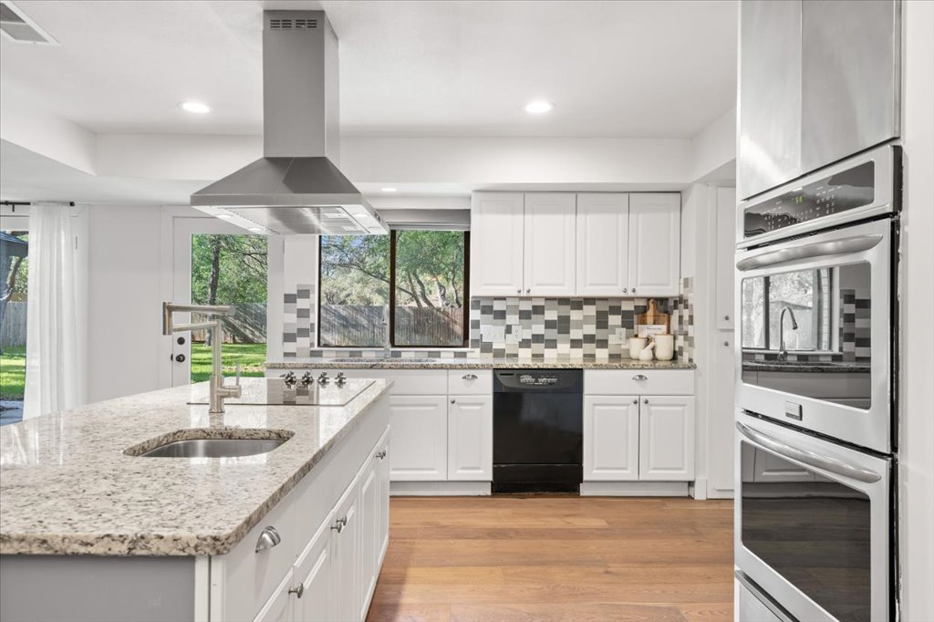 3402 Saddlestring Trail Austin, TX 78739 - Photo 4 of 33 Kitchen with black appliances, island exhaust hood, light stone countertops, white cabinets, and light wood-style floors
