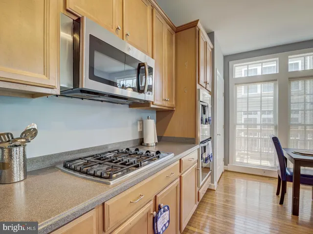 a kitchen with stainless steel appliances granite countertop a refrigerator a sink dishwasher a stove and a dining table with wooden floor