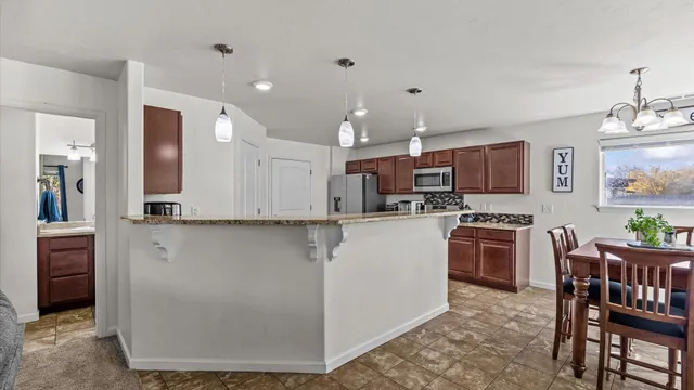 a kitchen with stainless steel appliances kitchen island granite countertop a refrigerator a stove top oven and a dining table with wooden floor