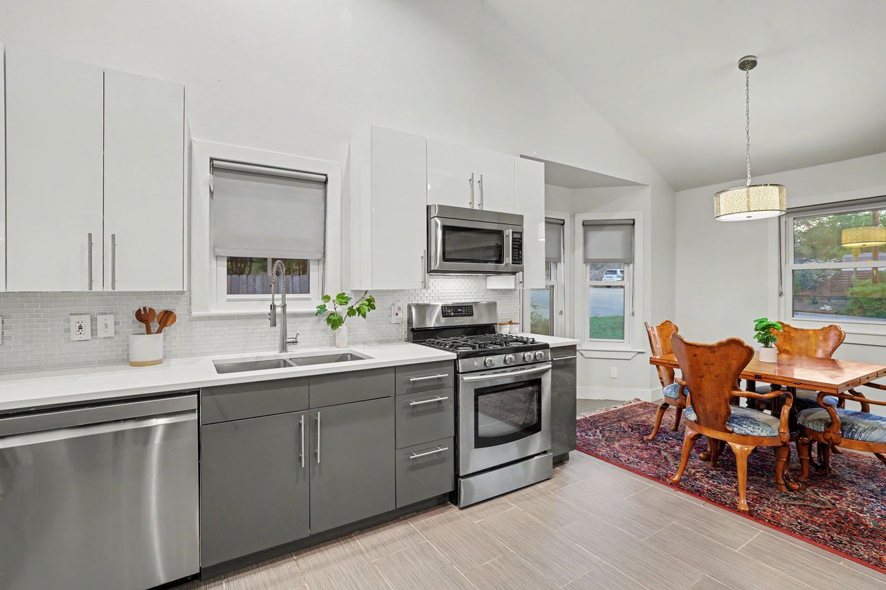 6903 Ardath Street Austin, TX 78757 - Photo 16 of 40 Two tone kitchen with two tone color scheme, stainless steel appliances, vaulted ceiling, decorative light fixtures, and tasteful backsplash