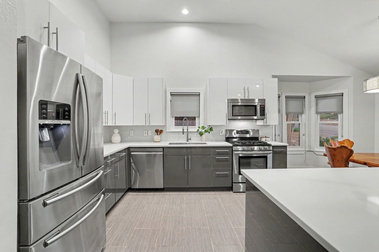 6903 Ardath Street Austin, TX 78757 - Photo 17 of 40 Kitchen featuring two tone cabinetry, stainless steel appliances, tasteful backsplash, modern cabinets, and vaulted ceiling
