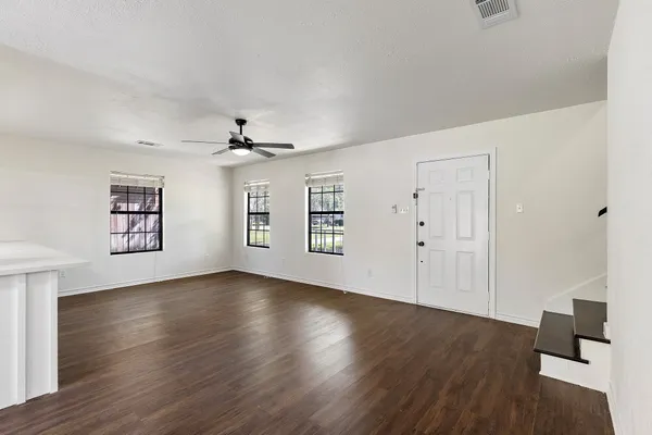an empty room with wooden floor chandelier and windows