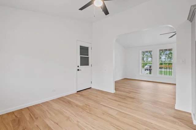 an empty room with wooden floor chandelier fan and windows