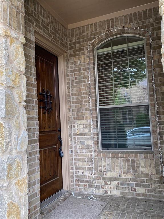 4679 Edith Street Plano, TX 75024 - Photo 5 of 34 Stone and brick facade with a solid wood front door featuring iron detailing, an arched window with blinds, and a textured concrete entry pad