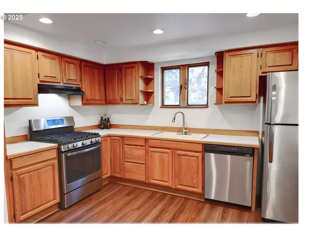 a kitchen with stainless steel appliances granite countertop a refrigerator a sink dishwasher a stove and white countertops with wooden floor