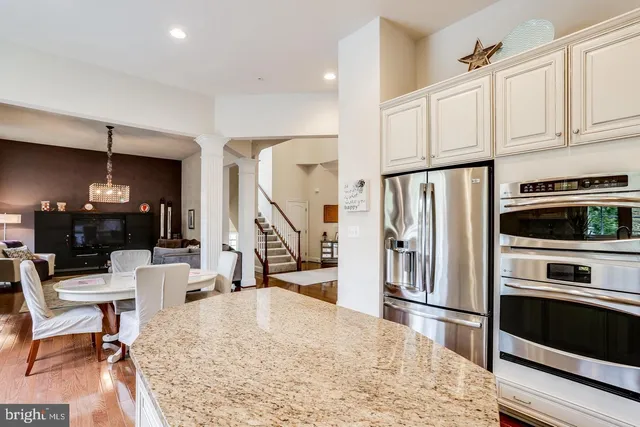 a kitchen with stainless steel appliances kitchen island granite countertop a refrigerator a stove a microwave oven a dining table and chairs with wooden floor