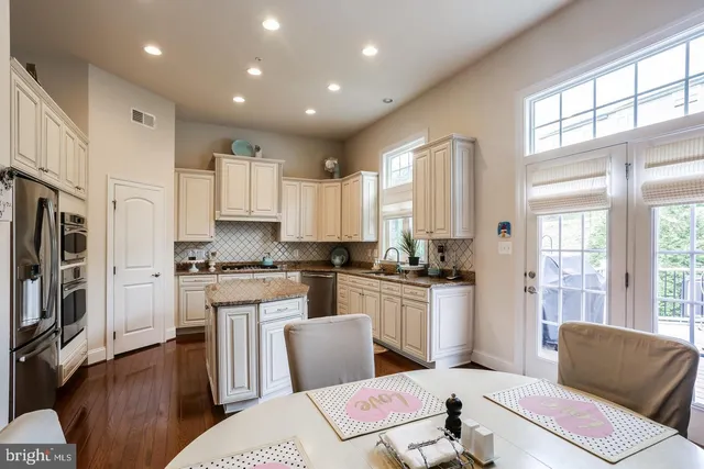 a kitchen with stainless steel appliances granite countertop a stove a refrigerator a sink dishwasher and white cabinets with wooden floor