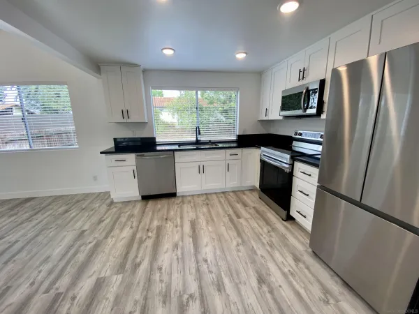 an empty room with wooden floor kitchen view and windows