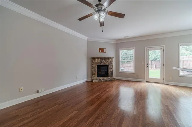 an empty room with wooden floor a ceiling fan a fireplace and windows