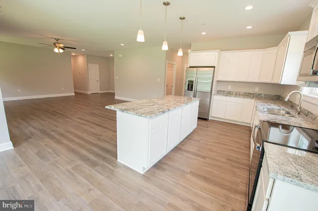 a large kitchen with kitchen island a stove a sink a refrigerator white cabinets and wooden floor