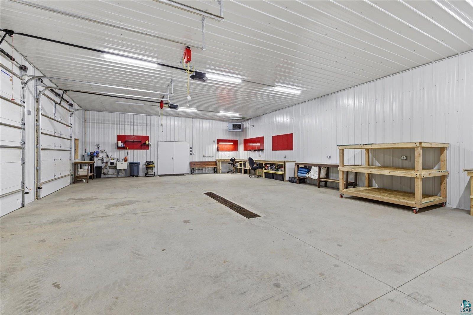 7185 Giants Ridge Road Embarrass, MN 55732 - Photo 43 of 47 Spacious workshop with concrete flooring, overhead fluorescent lighting, multiple overhead doors, white corrugated metal walls, and built-in workbench areas
