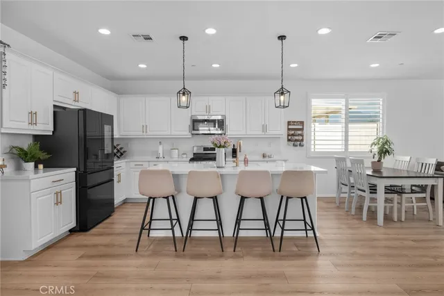 a kitchen with stainless steel appliances granite countertop a dining table chairs refrigerator and sink