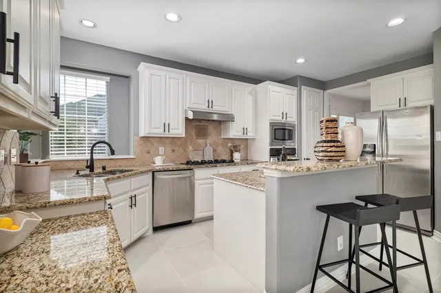 a kitchen with stainless steel appliances granite countertop a stove a sink a refrigerator white cabinets and wooden floor