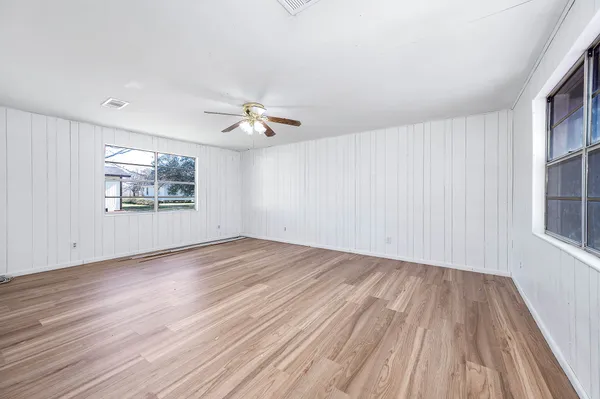 an empty room with wooden floor chandelier fan and windows