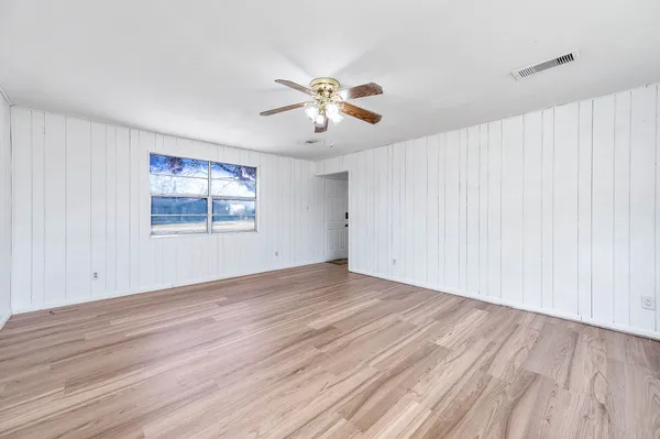 an empty room with wooden floor chandelier fan and windows