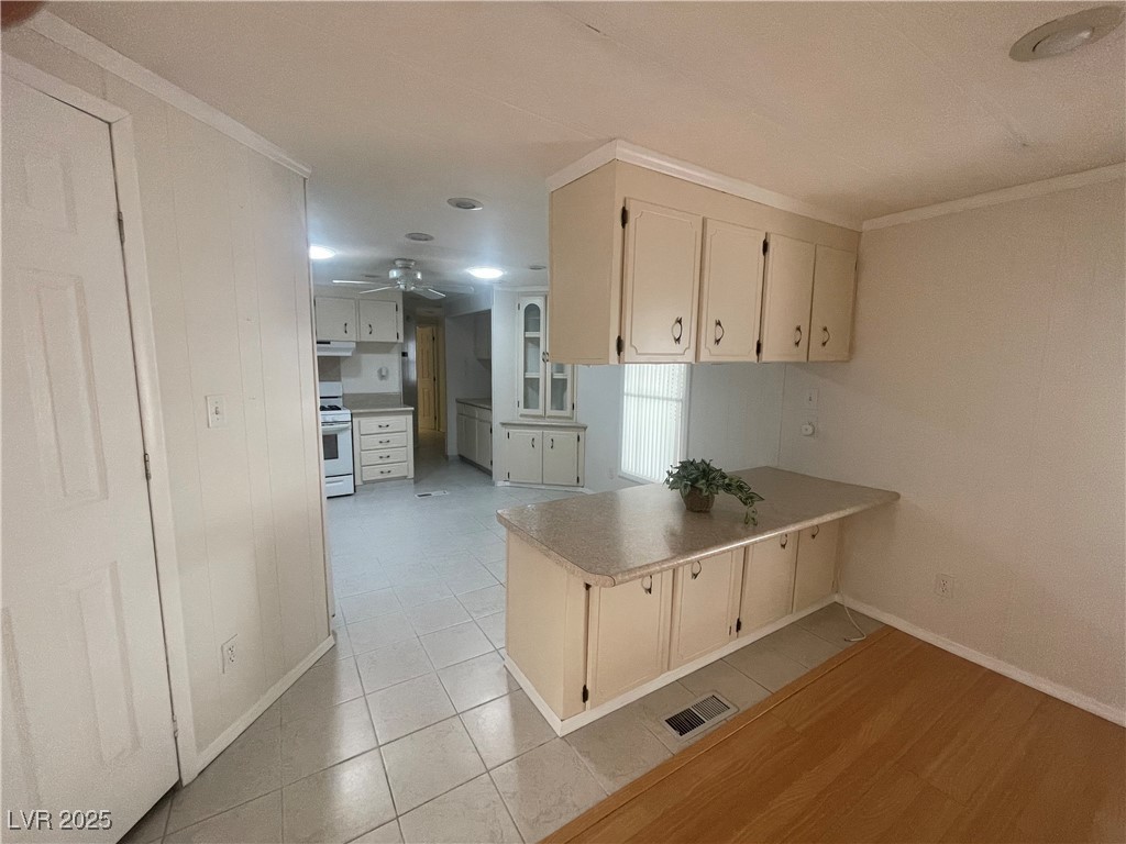 4641 Royal Ridge Boulevard Las Vegas, NV 89103 - Photo 14 of 38 Kitchen with crown molding, a peninsula, white range, light tile patterned floors, and ceiling fan