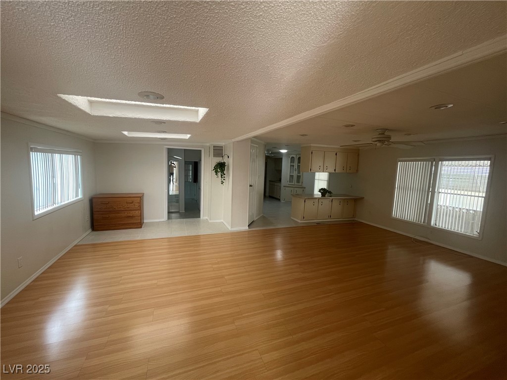 4641 Royal Ridge Boulevard Las Vegas, NV 89103 - Photo 6 of 38 Unfurnished living room with plenty of natural light, light wood-type flooring, a textured ceiling, crown molding, and a skylight