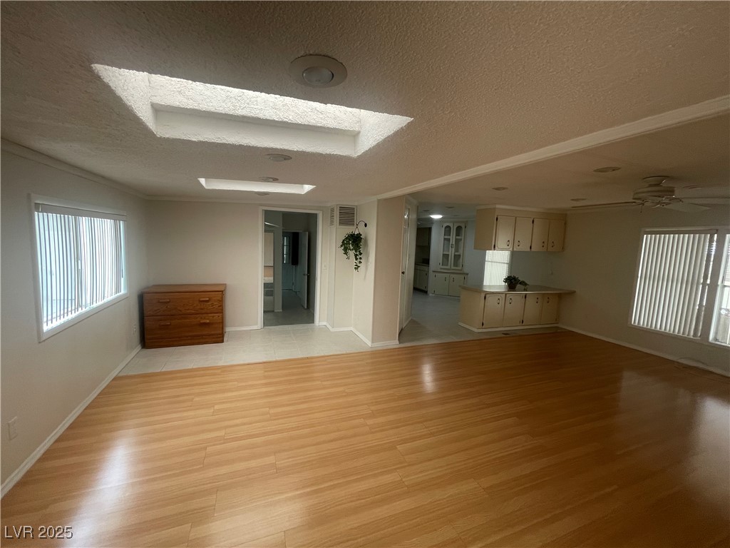 4641 Royal Ridge Boulevard Las Vegas, NV 89103 - Photo 7 of 38 Unfurnished living room with healthy amount of natural light, a textured ceiling, light wood-style floors, a skylight, and ceiling fan