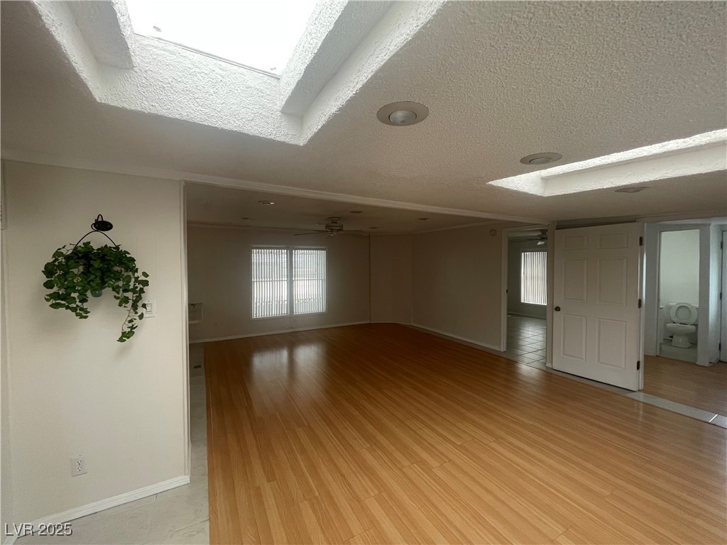 4641 Royal Ridge Boulevard Las Vegas, NV 89103 - Photo 8 of 38 Unfurnished room featuring a textured ceiling, a skylight, light wood-style flooring, and ceiling fan