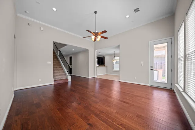 a view of an empty room with wooden floor and a ceiling fan