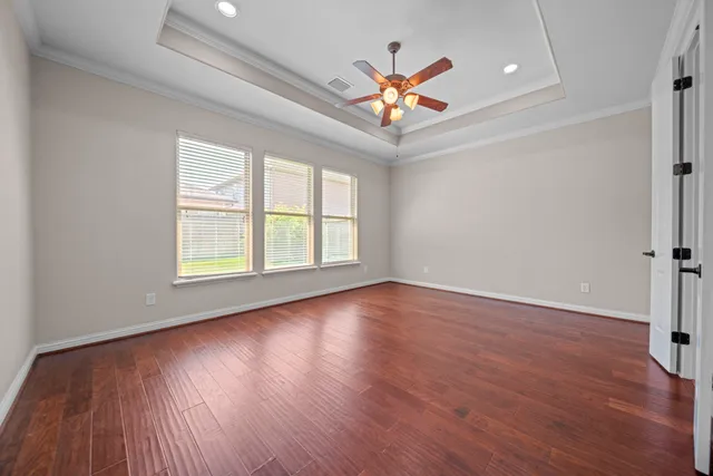 an empty room with wooden floor chandelier fan and windows