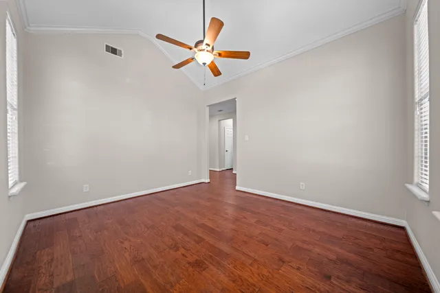 an empty room with wooden floor fan and windows