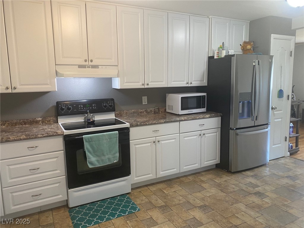 27 Carson Court Ely, NV 89301 - Photo 6 of 22 Kitchen with electric range oven, white microwave, stainless steel fridge with ice dispenser, under cabinet range hood, and white cabinets