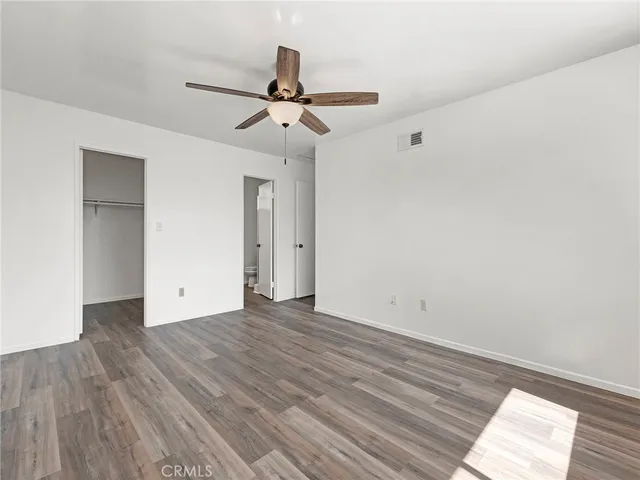 a view of an empty room with wooden floor and a ceiling fan
