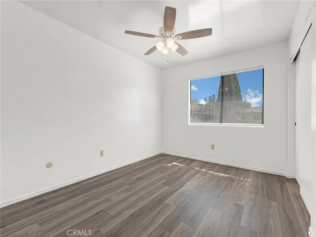 an empty room with wooden floor ceiling fan and windows