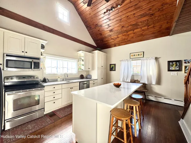 a open kitchen with stainless steel appliances kitchen island granite countertop a stove a sink dishwasher and white cabinets with wooden floor