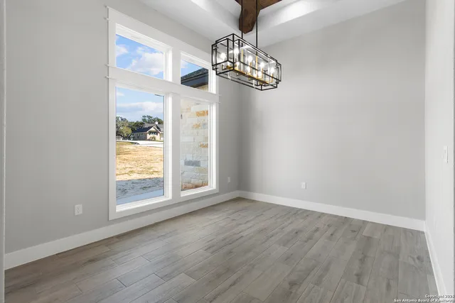 an empty room with wooden floor chandelier and windows