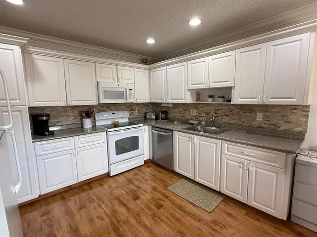 a white kitchen with granite top and stainless steel appliances