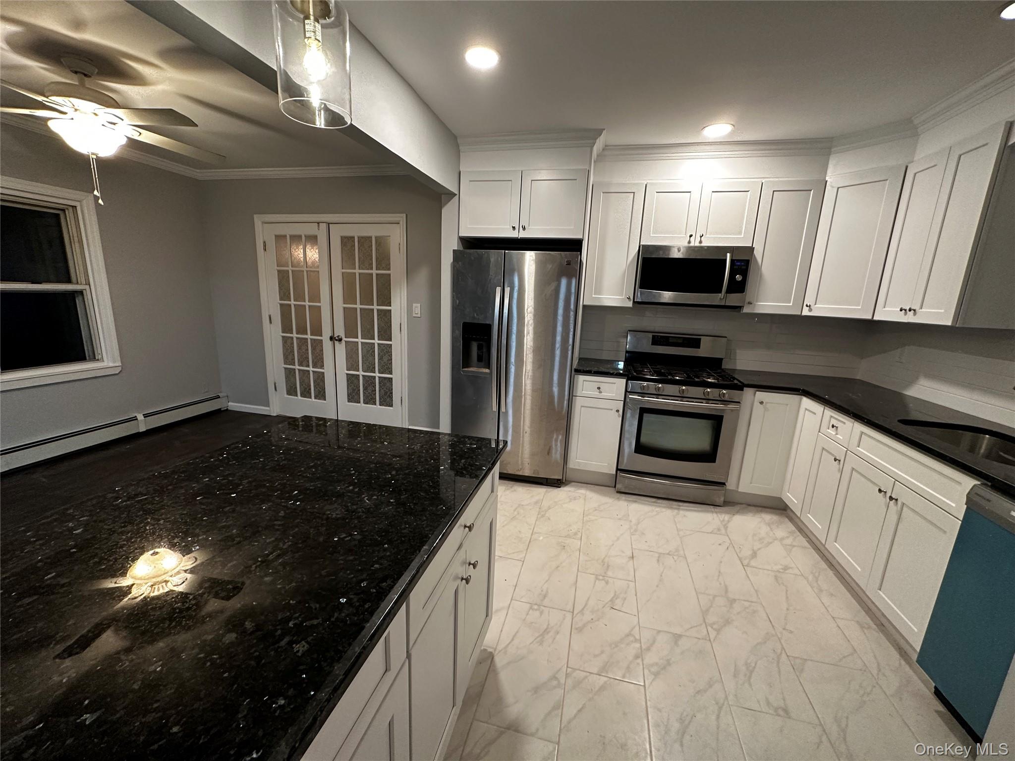 Kitchen featuring light marble finish flooring, stainless steel appliances, white cabinets, a baseboard radiator, and dark stone countertops
