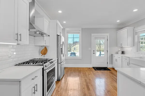 a kitchen with stainless steel appliances a stove a sink and white cabinets with wooden floor