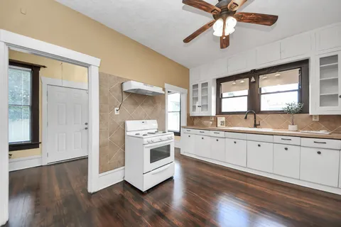 a large kitchen with granite countertop a stove a sink and white cabinets with wooden floor next to windows