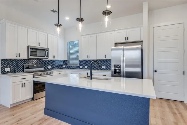 a kitchen with stainless steel appliances granite countertop a sink a stove a refrigerator cabinets and wooden floor