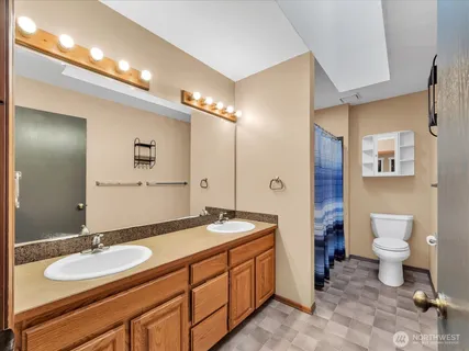 a spacious bathroom with a granite countertop sink toilet a mirror a vanity and shower