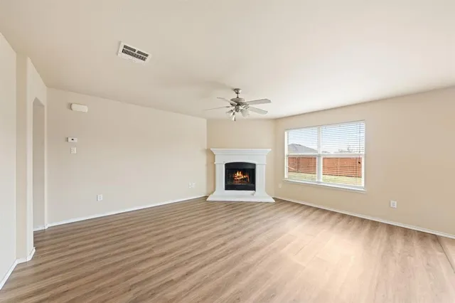 a view of an empty room with wooden floor fireplace and a window